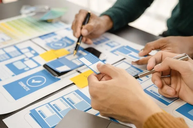 Equipo trabajando en prototipos y diseño de interfaces de usuario sobre una mesa con planos y notas adhesivas.